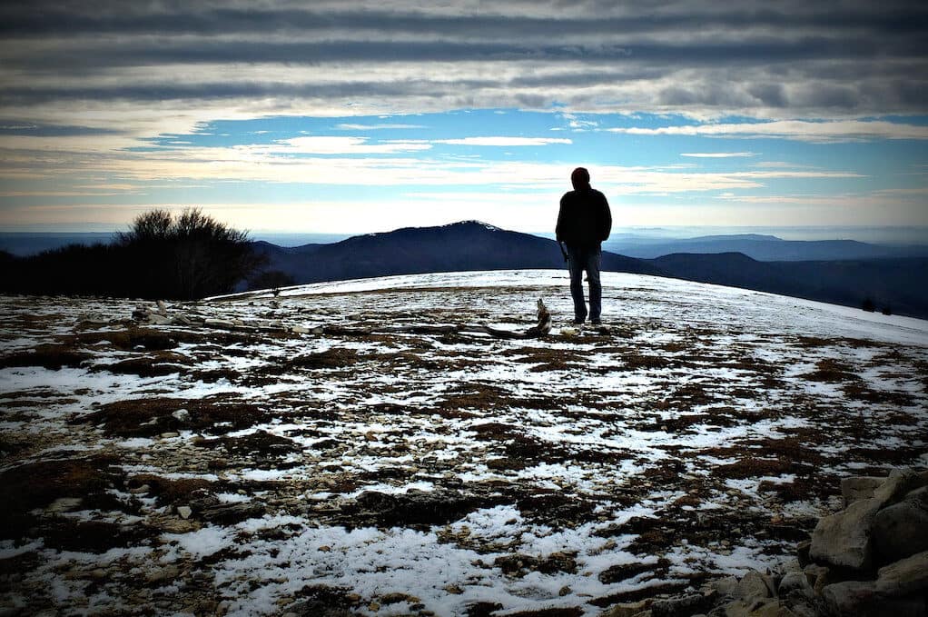 photo of solitary man looking at the mountains on the horizon