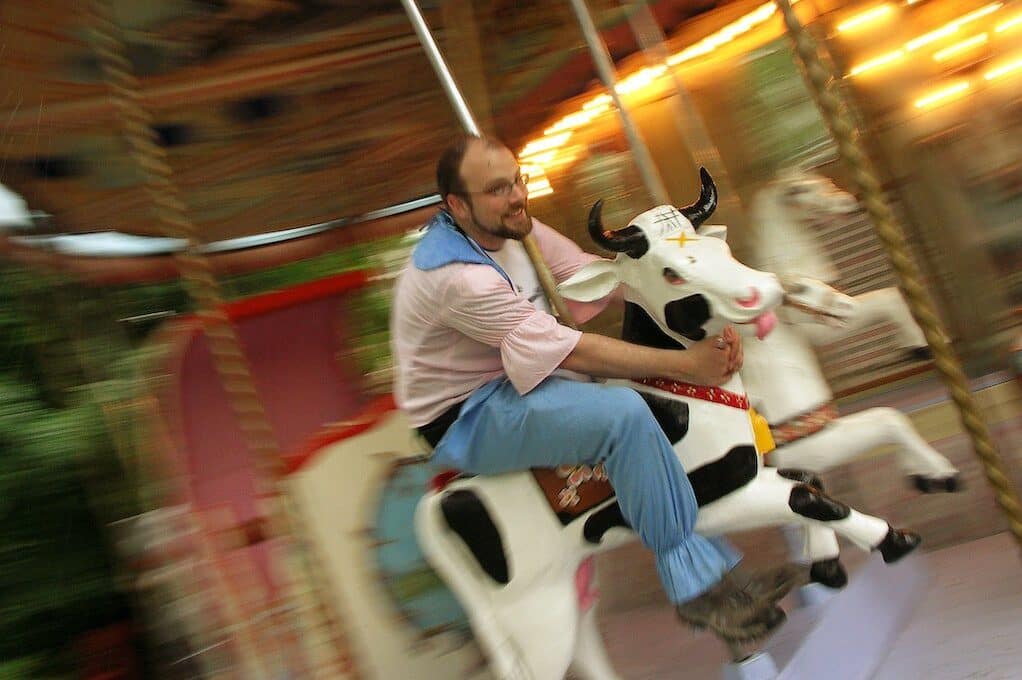 photo of man riding a cow on a merry-go-round