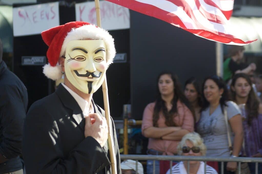 photo of person in Guy Fawkes mask carrying an American flag