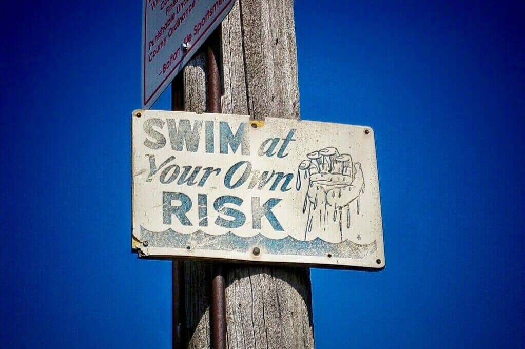 "Swim at your own risk" sign nailed to post