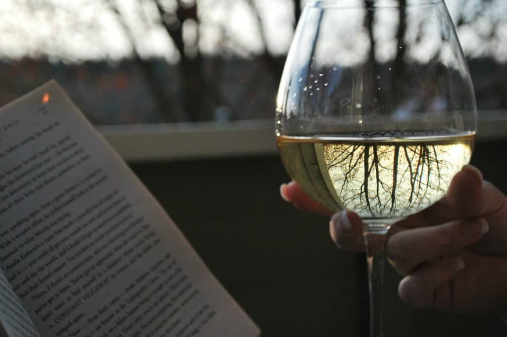 photo of someone holding wine glass and a book
