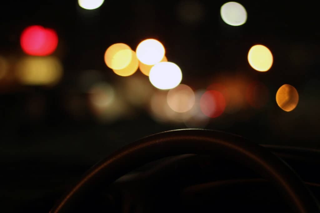 photo taken at night from interior of car of exterior lights with steering wheel in foreground