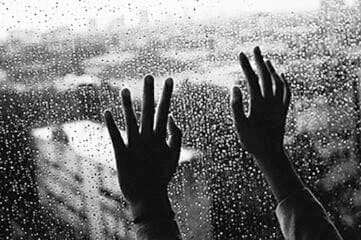 black and white photo of hands pressed up against the inside of a rainy window