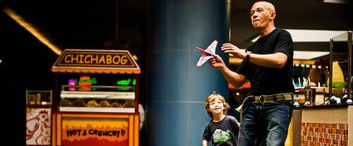 photo of man holding a toy plane in a mall with boy standing beside him